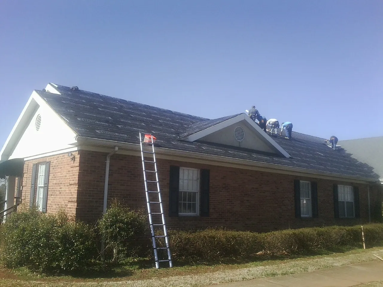 Crew tearing shingles off a brick ranch roof with a ladder set — Metal Roof Repair work by our crew in Canyon Creek