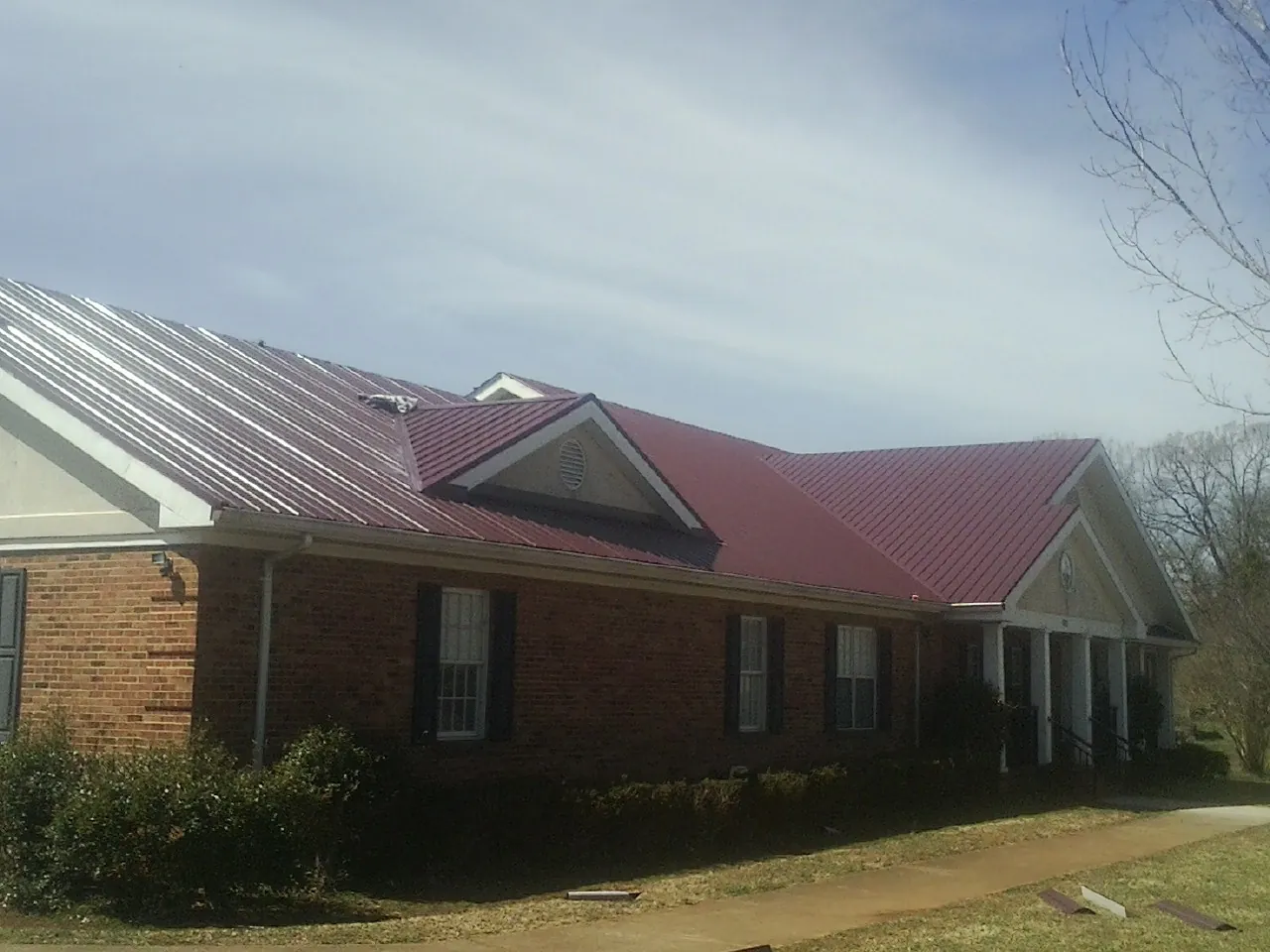 Red metal roof with gabled entries on a long brick building, from a Hail Damage Roof Repair job in Canyon Creek