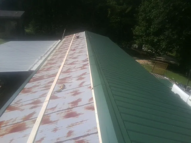 Old rusted panels beside newly installed green metal roofing — Wind Damage Roof Repair by Roofing Brothers in Canyon Creek