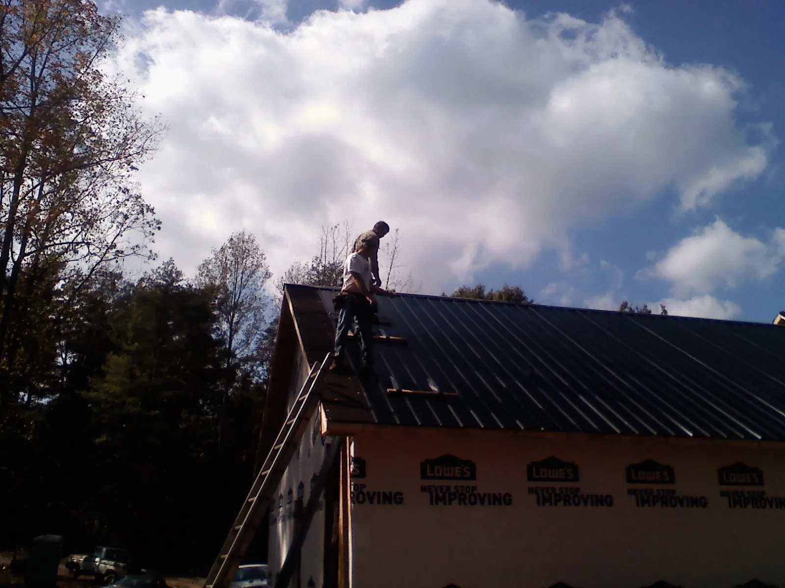 Roofer fastening dark metal panels high against a cloudy sky, from a Roof Inspection job in Canyon Creek