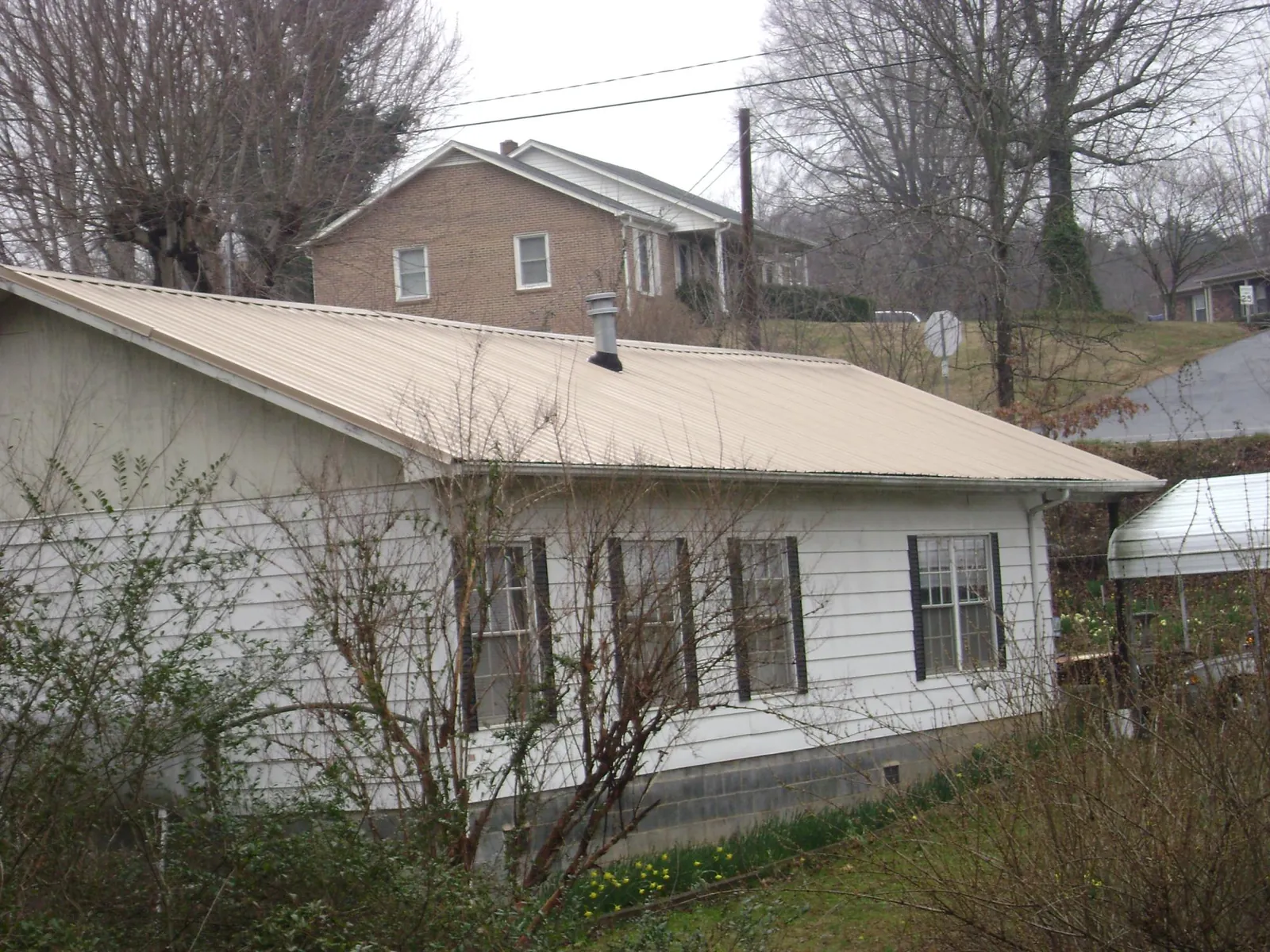 Tan metal roof on a white sided house set into a hillside — Commercial Roofing by Roofing Brothers in Canyon Creek